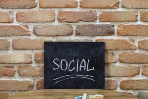 Chalk board with the word SOCIAL drown by hand and chalks on wooden table on brick wall background. photo