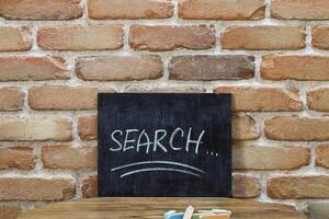 Chalk board with the word SEARCH drown by hand and chalks on wooden table on brick wall background. photo