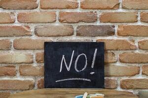 Chalk board with the word NO drown by hand and chalks on wooden table on brick wall background. photo