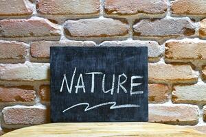 Chalk board with the word NATURE drown by hand and chalks on wooden table on brick wall background. photo