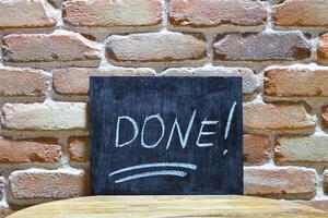 Chalk board with the word DONE drown by hand and chalks on wooden table on brick wall background. photo