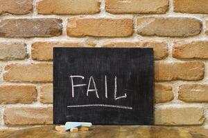 Chalk board with the word FAIL drown by hand and chalks on wooden table on brick wall background. photo