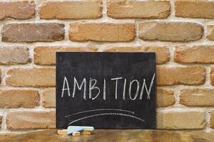Chalk board with the word AMBITION drown by hand and chalks on wooden table on brick wall background. photo