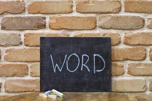 Chalk board with the word WORD drown by hand and chalks on wooden table on brick wall background. photo
