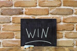 Chalk board with the word WIN drown by hand and chalks on wooden table on brick wall background. photo