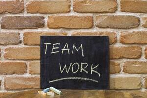 Chalk board with the word TEAMWORK drown by hand and chalks on wooden table on brick wall background. photo