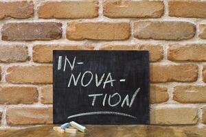 Chalk board with the word INNOVATION drown by hand and chalks on wooden table on brick wall background. photo
