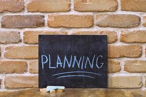 Chalk board with the word PLANNING drown by hand and chalks on wooden table on brick wall background. photo
