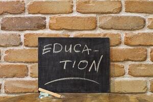 Chalk board with the word EDUCATION drown by hand and chalks on wooden table on brick wall background. photo