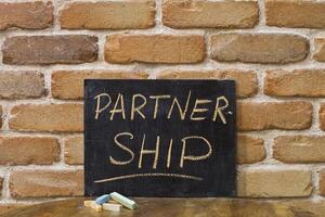 Chalk board with the word PARTNERSHIP drown by hand and chalks on wooden table on brick wall background. photo