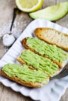 Croutons with avocado guacamole on white plate closeup on rustic wooden table. photo