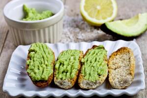 Fresh crostini with avocado guacamole on white plate closeup on rustic wooden table. photo