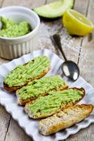 Toasts with avocado guacamole on white plate closeup on rustic wooden table. Diet breakfast. photo