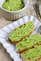 Fresh crostini with avocado guacamole on white plate closeup on rustic wooden table. photo