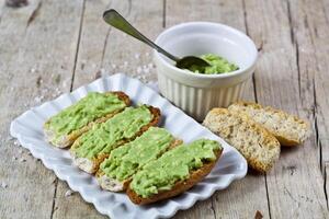 Crostini with avocado guacamole on white plate closeup on rustic wooden table. Diet breakfast. photo