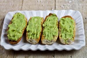 Fresh crostini with avocado guacamole on white plate closeup on rustic wooden table. photo