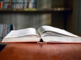 An open book or textbook vintage style on wooden table in the library and the bookshelves background.Education learning concept photo