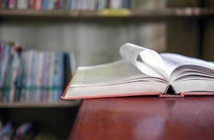 An open book or textbook vintage style on wooden table in the library and the bookshelves background.Education learning concept photo
