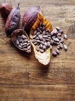 Top view of brown cocoa beans on dry cocoa leaf and dry cacao pod on a rustic wooden table. photo