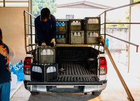 Workers lift drinking water bottles in crates into the back of a transport truck purified drinking water inside the production line to prepare for sale. Water drink factory, small business photo