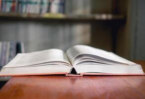 An open book or textbook vintage style on wooden table in the library and the bookshelves background.Education learning concept photo