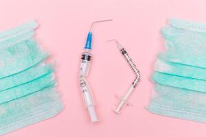 Anti Vaccine Movement and Anti Mask Concept - Broken Medical Syringe and Green Torn Medical Face Mask on the Pink Background. Pandemic and Lockdown End - Top View, Flat Lay photo