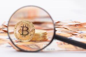 A Stack of Bitcoin Coins Visible Through a Magnifying Glass on the 50-Euro Banknotes. Euro Currency and Crypto Currency. Orange Paper Money. A Lot of Fifty-Euro Bills. Anonymous Payments Concept photo