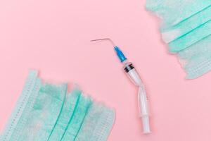 Anti Vaccine Movement and Anti Mask Concept - Broken Medical Syringe and Green Torn Medical Face Mask on the Pink Background. Pandemic and Lockdown End - Top View, Flat Lay photo