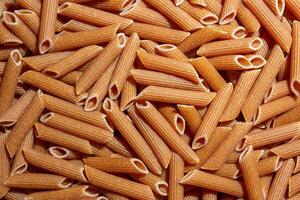 Uncooked Whole Grain Penne Rigate Pasta. A Culinary Canvas of Whole Wheat Macaroni, Creating a Lively and Textured Background for Gourmet Cooking. Whole Grain Dry Pasta. Whole Wheat Raw Macaroni photo