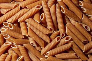 Uncooked Whole Grain Penne Rigate Pasta. A Culinary Canvas of Whole Wheat Macaroni, Creating a Lively and Textured Background for Gourmet Cooking. Whole Grain Dry Pasta. Whole Wheat Raw Macaroni photo