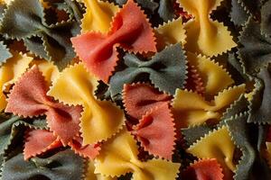 Uncooked Vibrant Colored Farfalle Pasta. A Culinary Canvas of Multicolored Bow-Tie Macaroni, Creating a Lively and Textured Background for Gourmet Cooking Enthusiasts. Colored Dry Pasta. Raw Macaroni photo