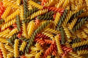 Uncooked Vibrant Colored Fusilli Pasta. A Mesmerizing Culinary Canvas of Multicolored Spirals, Creating a Lively and Textured Background for Gourmet Cooking. Colored Dry Pasta. Raw Macaroni photo