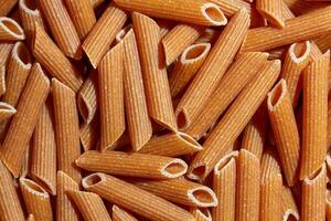 Uncooked Whole Grain Penne Rigate Pasta. A Culinary Canvas of Whole Wheat Macaroni, Creating a Lively and Textured Background for Gourmet Cooking. Whole Grain Dry Pasta. Whole Wheat Raw Macaroni photo