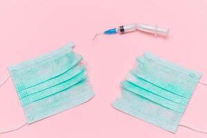 Anti Vaccine Movement and Anti Mask Concept - Broken Medical Syringe and Green Torn Medical Face Mask on the Pink Background. Pandemic and Lockdown End - Top View, Flat Lay photo
