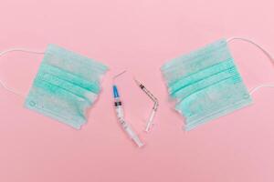 Anti Vaccine Movement and Anti Mask Concept - Broken Medical Syringe and Green Torn Medical Face Mask on the Pink Background. Pandemic and Lockdown End - Top View, Flat Lay photo