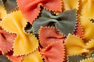 Uncooked Vibrant Colored Farfalle Pasta. A Culinary Canvas of Multicolored Bow-Tie Macaroni, Creating a Lively and Textured Background for Gourmet Cooking Enthusiasts. Colored Dry Pasta. Raw Macaroni photo
