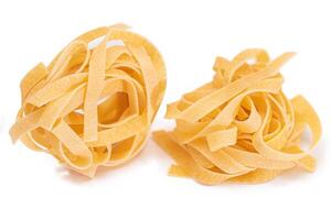 Two Classic Italian Raw Egg Fettuccine - Isolated on White Background. Dry Twisted Uncooked Pasta. Italian Culture and Cuisine. Raw Golden Macaroni Pattern - Isolation photo