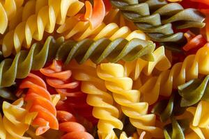 Uncooked Vibrant Colored Fusilli Pasta. A Mesmerizing Culinary Canvas of Multicolored Spirals, Creating a Lively and Textured Background for Gourmet Cooking. Colored Dry Pasta. Raw Macaroni photo