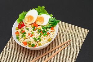 Beautiful Noodle Dish with Green Pea, Carrot, Eggs, Red Hot Pepper and Greens on Sushi Mat. Instant Noodles with Vegetables photo