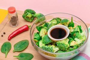 Fresh Green Salad of Avocado, Broccoli, Spinach and Cucumber with Soy Sauce and Red Hot Pepper on Wooden Cutting Board. Vegan Salad. Vegetarian Culture. Raw Food. Healthy Eating and Vegetable Diet photo
