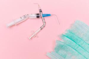 Anti Vaccine Movement and Anti Mask Concept - Broken Medical Syringe and Green Torn Medical Face Mask on the Pink Background. Pandemic and Lockdown End - Top View, Flat Lay photo