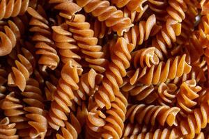 Uncooked Whole Grain Fusilli Pasta. A Culinary Canvas of Whole Wheat Spirals, Creating a Lively and Textured Background for Gourmet Cooking. Whole Grain Twisted Dry Pasta. Whole Wheat Raw Macaroni photo