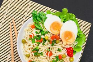 Beautiful Noodle Dish with Green Pea, Carrot, Eggs, Red Hot Pepper and Greens on Sushi Mat. Instant Noodles with Vegetables photo