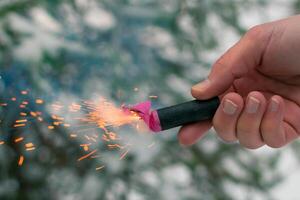 Burning Firecracker in a Hand. Guy Holding a Petard Outdoors in Winter at Daytime. Loud and Dangerous New Year's Entertainment. Hooliganism with Pyrotechnics. Noise of Firecrackers in Public Places photo