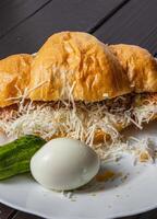 Croissant sandwich with tuna, egg and cucumber on a white plate on a dark table photo