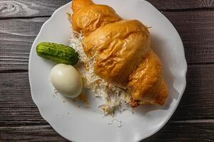croissant sandwich with tuna, egg, cucumber on a white plate on a wooden table photo