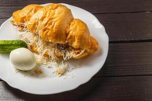croissant sandwich with tuna, egg, cucumber on a white plate on a wooden table photo