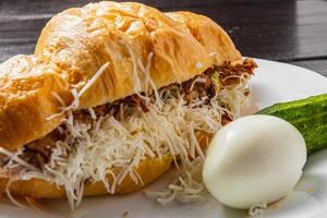 Croissant sandwich with tuna on a white plate on a dark table close up side view photo