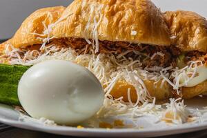 Croissant sandwich with tuna, egg, cucumber on a white plate, close up view photo