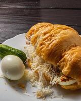 Croissant sandwich with tuna, egg, cucumber and cheese on a white plate photo